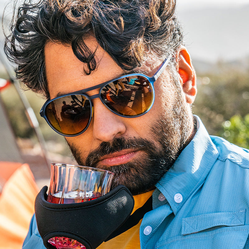 Ein bärtiger Mann mit blauer Pilotensonnenbrille schnuppert an Whiskey aus einer Glashalterung, die man auch in einem Skymall-Katalog sehen könnte.