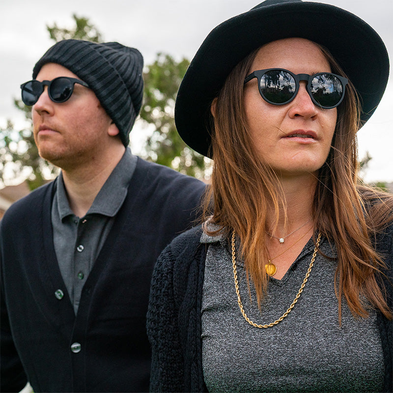 Ein Hipster-Mann und eine Hipster-Frau in schicken schwarzen Outfits tragen eine runde schwarze Sonnenbrille mit nicht reflektierenden schwarzen Gläsern.
