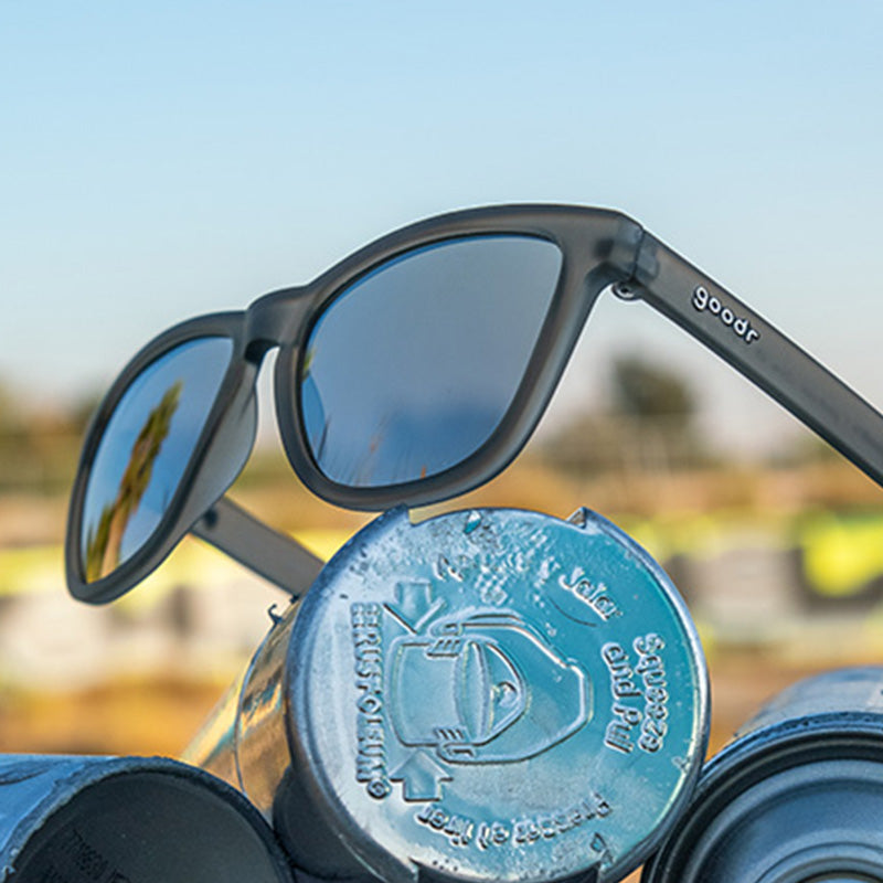 Dreiviertelansicht einer grauen aktiven Sonnenbrille mit grauen Gläsern, die auf einer Flasche mit silberner Sprühfarbe sitzt.