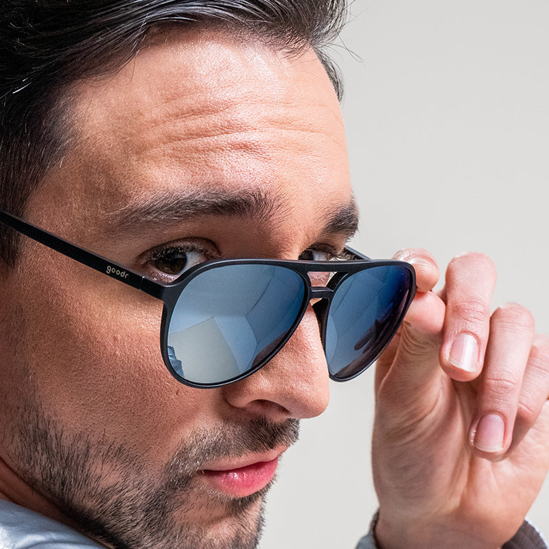 Ein Mann blickt über die Schulter, die schwarz-verchromte Flieger-Sonnenbrille ist ihm auf die Nase gerutscht.