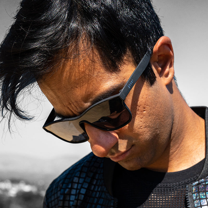 Ein Mann mit einer schwarzen, flachen Sonnenbrille mit einfachen Gläsern blickt entschlossen zur Seite.